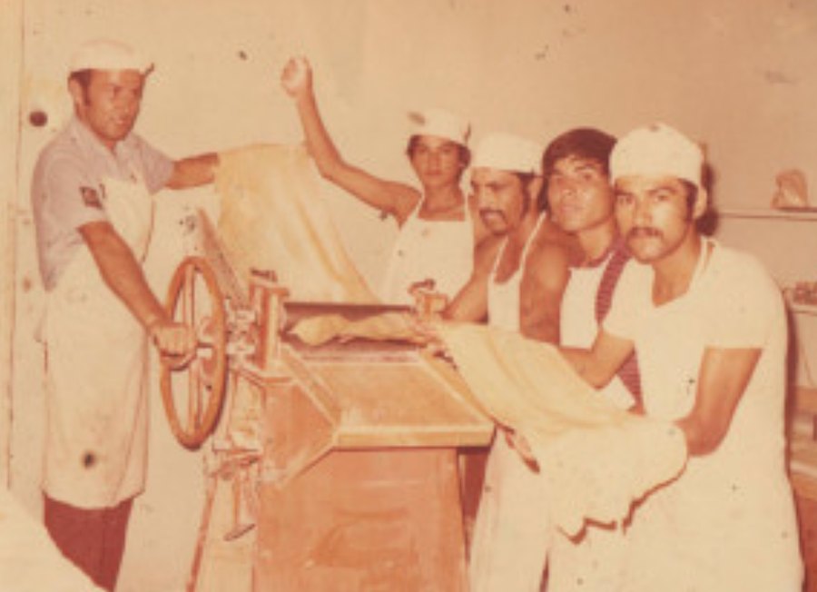 Foto antigua de cinco dulceros pasando la masa por una laminadora a manivela